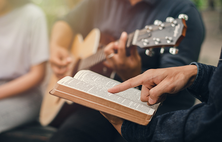 A young boy reads the Bible while his friend plays the guitar. when he worships God A small group of Christians or concepts in a church at a church.
